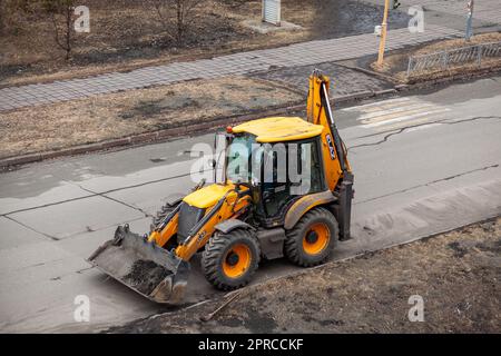 26.04.2023, Kemerovo, Russia. Un trattore giallo è in piedi o sta guidando su strada per lavori su strada. Pulizia stradale con un trattore Foto Stock