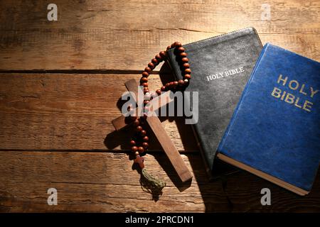 Sacre Bibbie con perline di preghiera e croce su sfondo ligneo Foto Stock