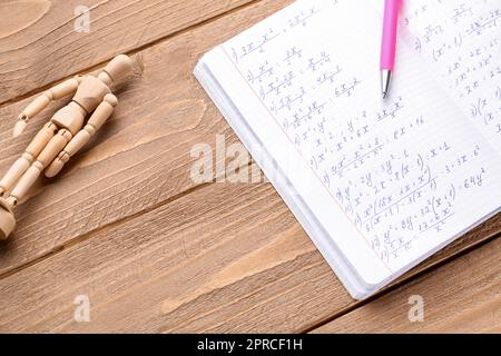 Copybook con formule matematiche, penna e manichino su sfondo di legno Foto Stock
