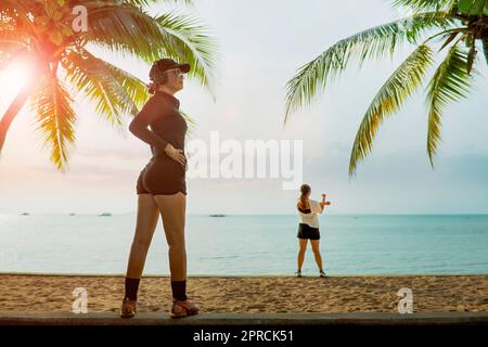 due donne che si allungano scaldano prima di allenarsi in spiaggia Foto Stock
