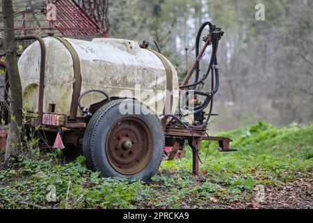Piccolo serbatoio di plastica agricola d'annata per l'acqua o fertilizzanti artificiali parcheggiati nei boschi. Ruote arrugginite testimoniano la sua età. Foto Stock