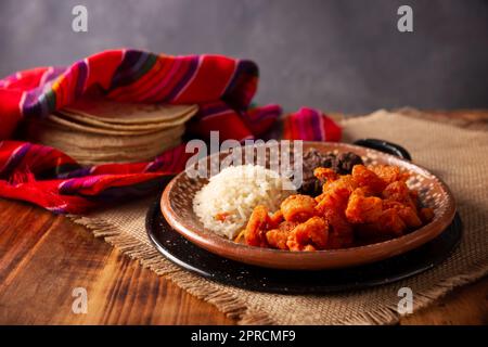 Crostini di maiale stufati in salsa rossa accompagnati da riso e fagioli fritti. Piatto tradizionale fatto in casa molto popolare in Messico, questo piatto è parte del popul Foto Stock