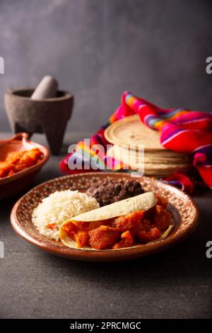 Croste di maiale in salsa rossa Taco accompagnato da riso e fagioli fritti. Piatto tradizionale fatto in casa molto popolare in Messico, questo piatto è parte del popolare Foto Stock