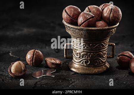 Noci di macadamia in ciotola d'ottone vintage su sfondo scuro Foto Stock