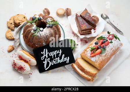 Tavolo da dessert con vari tipi di torte, pezzetti di torte, dolci, biscotti con condimenti di frutta su sfondo bianco. Vista dall'alto. Foto Stock