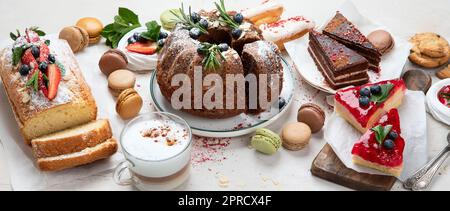 Tavolo da dessert con vari tipi di torte, pezzetti di torte, dolci, biscotti con condimenti di frutta su sfondo bianco. Vista dall'alto. Panorama. Foto Stock