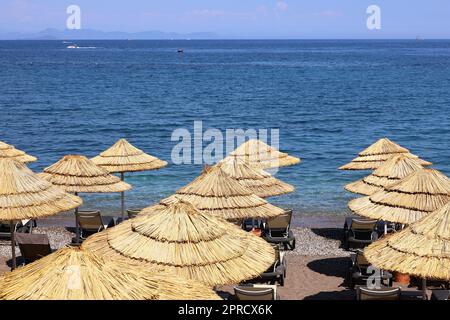 Spiaggia vuota con ombrelloni in vimini e sedie a sdraio. Pittoresca vista sul mare blu e le montagne nella nebbia, resort di lusso Foto Stock