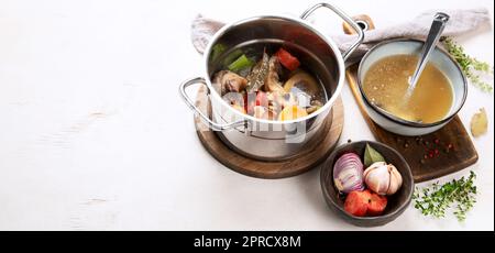 Brodo di manzo di carne di manzo su ossa cotto lentamente con verdure: Carota, cipolla, aglio e spezie servito in una pentola su sfondo bianco con ingredienti Foto Stock