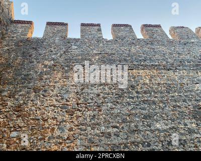 Grande muro di pietra di un'antica fortezza medievale fatta di ciottoli contro un cielo blu. Foto Stock