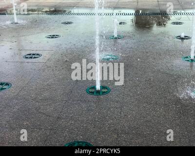 Una piccola bella fontana cantata all'aperto, sulla strada. Gocce d'acqua, getti d'acqua congelati nell'aria in volo contro lo sfondo di Foto Stock