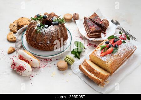 Tavolo da dessert con vari tipi di torte, pezzetti di torte, dolci, biscotti con condimenti di frutta su sfondo bianco. Vista dall'alto. Foto Stock