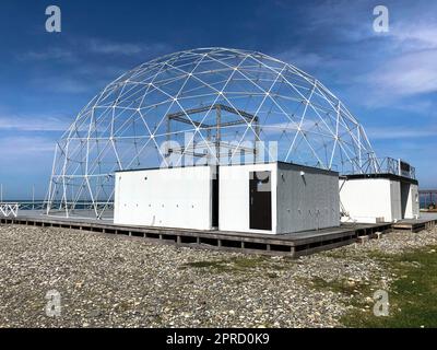 Sferico rotondo astratto costruzione costruzione metallo bianco di triangoli su una spiaggia sabbiosa contro il mare e il cielo blu. Foto Stock