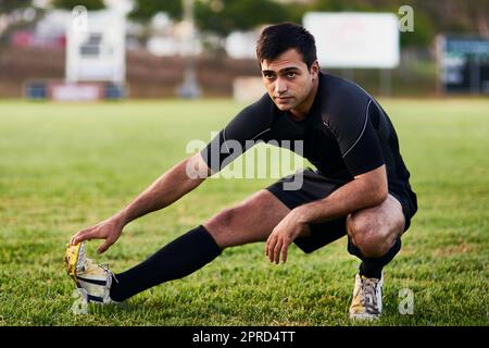 L'allungamento è la chiave. Scatto completo di un bel giovane sportivo che si allunga da solo prima di una pratica di rugby durante il giorno. Foto Stock