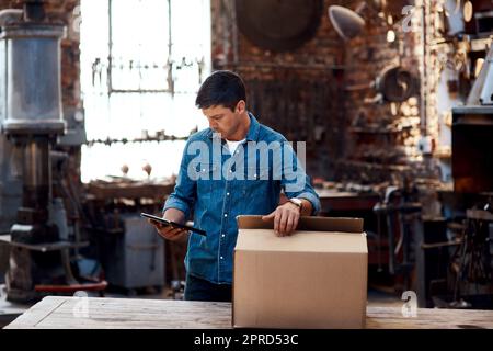 Im in attesa di più consegne in arrivo oggi. Un giovane uomo d'affari che utilizza un tablet digitale ordinando gli ordini e le consegne all'interno della sua officina. Foto Stock