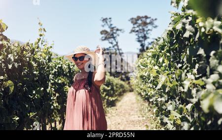 Questa vacanza è proprio quello di cui avevo bisogno: Una giovane donna felice che cammina attraverso un vigneto in una giornata di sole. Foto Stock