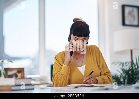 Questo è 21st secolo di affari. Attraente giovane donna d'affari seduta da sola nel suo ufficio che parla sul suo cellulare mentre scrive le note. Foto Stock