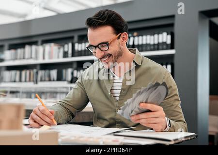 Sono troppo bravo a questo lavoro. Un bel giovane architetto maschile sorridente mentre lavorava con alcuni progetti in un ufficio moderno. Foto Stock