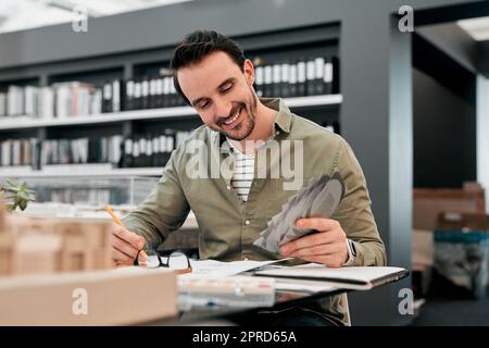 Ogni cosa che si unisca proprio come ho previsto. Un bel giovane architetto maschile sorridendo mentre lavorava con alcuni progetti in un ufficio moderno. Foto Stock