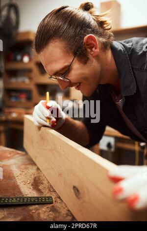 Facendo il mio marchio. Un carpentiere giovane messo a fuoco che fa le misure su un pezzo di legno all'interno di un'officina di notte. Foto Stock