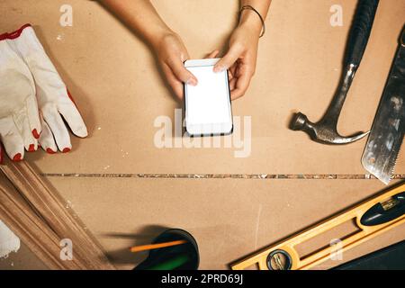 Basta fare una breve pausa. Scatto ad angolo alto di un falegname irriconoscibile testando sul suo cellulare all'interno di un laboratorio di notte. Foto Stock