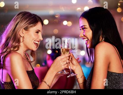 Heres alla nostra seconda. Due giovani donne allegre che hanno un brindisi celebrativo con bevande all'interno di un bar di notte. Foto Stock