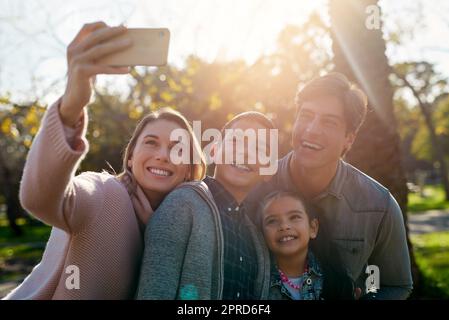 I momenti della nostra famiglia diventano i nostri ricordi più belli: Una giovane e felice famiglia che prende insieme un selfie nel parco. Foto Stock