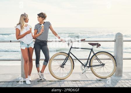 Due amici mangiano gelato mentre si alza sul lungomare con una bicicletta. Foto Stock