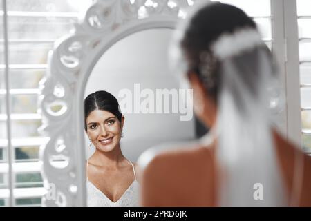 Il grande giorno è finalmente arrivato. Ripresa retroguide di una giovane sposa attraente che guarda nello specchio mentre si prepara per la sua cerimonia nuziale. Foto Stock