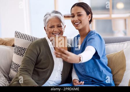 Un'infermiera giovane che prende selfie con una donna anziana in una casa di riposo, aggiunge una scintilla di gioia alla sua giornata. Foto Stock