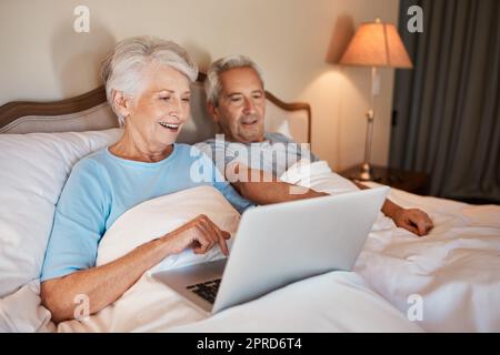 Grazie alla tecnologia è più facile condividere le fotografie. Una donna anziana felice che usa un computer portatile e si siede a letto con il marito a casa. Foto Stock