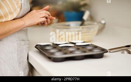Chi non ama la cottura. Una donna irriconoscibile che mette i portabicchieri in una teglia per muffin. Foto Stock