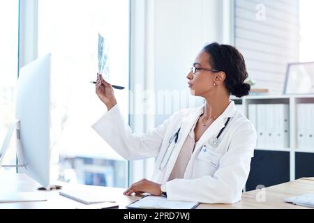 Un medico giovane che legge i risultati di una radiografia nella sua sala di consulenza. Foto Stock