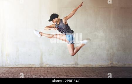 Saltare a nuove vette nella danza. Scatto a tutta lunghezza di una giovane donna attraente che salta e fa una mezza divisione come parte di una routine di danza. Foto Stock