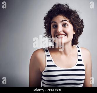 Eccitati. Studio girato di una giovane donna attraente che grinning ampiamente mentre in piedi su uno sfondo grigio. Foto Stock