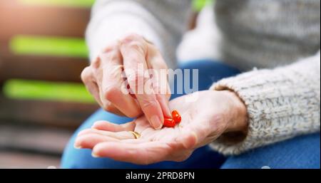 Questo mi farà sentire meglio: Una donna anziana irriconoscibile che sta per prendere medicinali fuori in un parco durante il giorno. Foto Stock