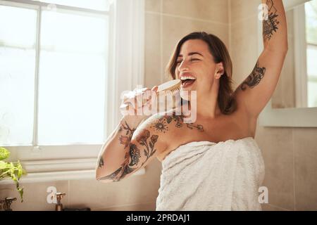 Inizia ogni giorno con una canzone nel tuo cuore. Una giovane donna attraente che canta mentre passa attraverso la sua routine di bellezza mattutina a casa. Foto Stock