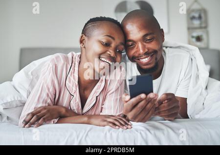 Un po' di tempo per iniziare la giornata. Una giovane coppia felice che usa uno smartphone in camera da letto a casa. Foto Stock