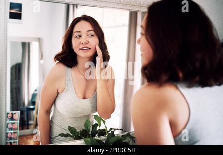 Tutto sembra così liscio. Una giovane donna attraente che ispeziona il suo viso mentre si alza davanti allo specchio nella sua camera da letto a casa. Foto Stock