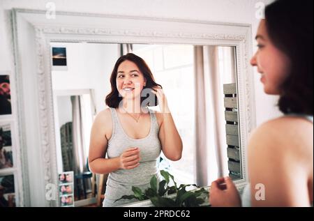 Im vivere per il modo in cui guardo proprio ora. Una giovane donna attraente che si guarda mentre si sta in piedi davanti allo specchio nella sua camera da letto a casa. Foto Stock