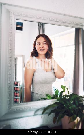 Vedo solo una bella ragazza in questo specchio, una giovane donna attraente che si guarda mentre si alza davanti allo specchio nella sua camera da letto a casa. Foto Stock