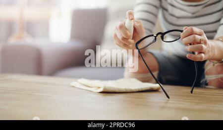 Pulire regolarmente per una visione chiara. Una donna irriconoscibile che pulisce i suoi occhiali da lettura a casa. Foto Stock