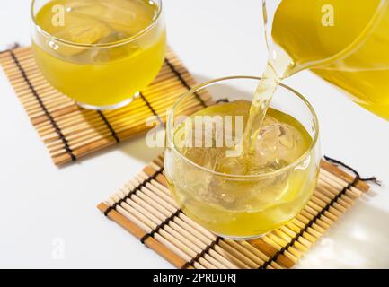 Versare il tè verde in un bicchiere da tè pieno di ghiaccio. Foto Stock