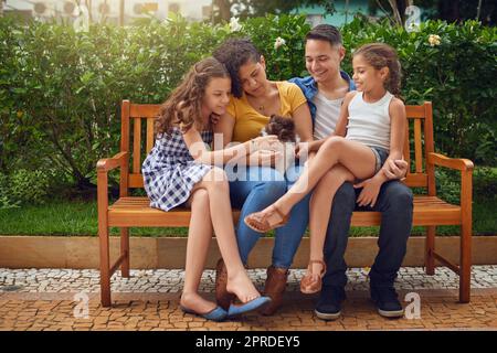 Tutti amiamo il nostro piccolo pooch. Scatto completo di una famiglia felice che gioca con il cane su una panchina al parco. Foto Stock