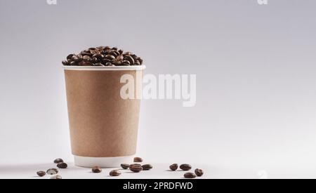 Si riuniscono per il caffè. Scatto da studio di una tazza di carta riempita con chicchi di caffè su sfondo grigio. Foto Stock