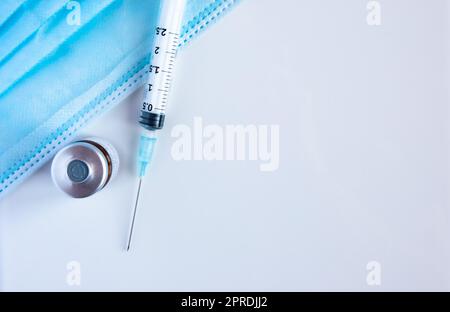Un flacone di vaccino con siringa e maschere chirurgiche. Foto Stock