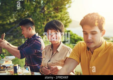 Tutti sono pronti a tuffarsi. Un gruppo di amici che gustano un pasto e bevono insieme intorno a un tavolo in una riunione all'aperto. Foto Stock