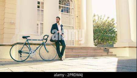 HES è sempre il primo ad arrivare. Foto a tutta lunghezza di un bel giovane uomo d'affari che si posa accanto a una bicicletta in città. Foto Stock