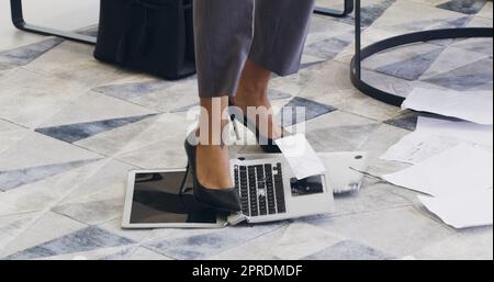 Shes aveva abbastanza tecnologia. Una donna d'affari irriconoscibile che rompeva un notebook saltando su di esso in un ufficio. Foto Stock