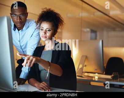 Un po' di lavoro straordinario. Due uomini d'affari che lavorano insieme di notte su un computer in un ufficio. Foto Stock