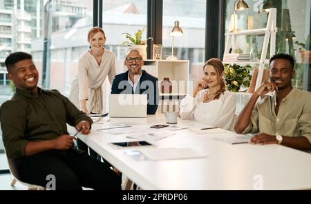 Team di marketing sorridente, diversificato e creativo seduti in una sala riunioni per aziende o startup. Nuovi giovani felici che ricevono coaching da imprenditori leader maturi che utilizzano un notebook Foto Stock